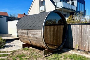 En rund trækonstruktion med et metal tag, placeret udendørs med et træhegn og et hus i baggrunden.