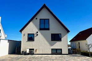 Et moderne hus i to etager med sadeltag, en balkon og en patio med udendørs møbler.