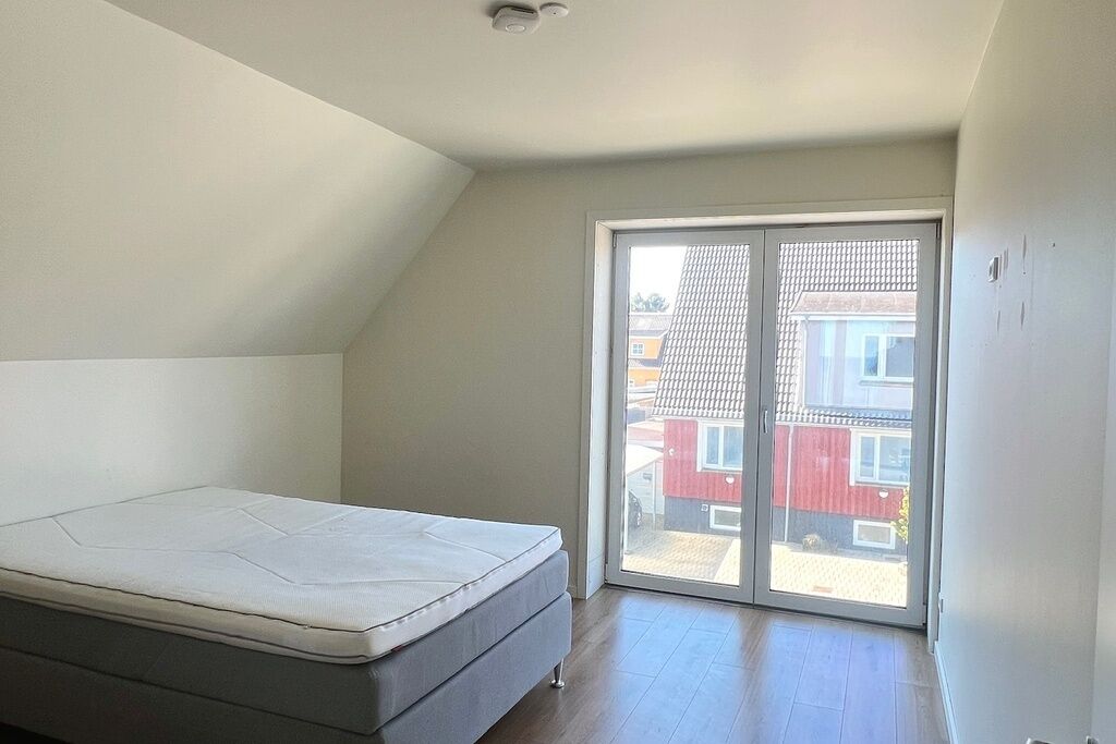 Un dormitorio con una cama individual, una puerta corrediza de vidrio a un balcón y un techo inclinado.