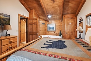 Una habitación con paneles de madera, una cama, un aparador, una lámpara y un cuadro en la pared.