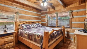 Un dormitorio tipo cabaña de troncos con una cama de madera, un ventilador de techo y una ventana con cortinas.