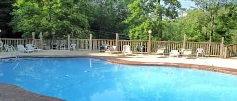 Une piscine avec une terrasse en bois, entourée d’arbres.