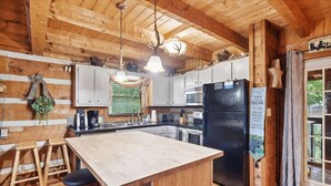 Un interior de madera con zona de cocina, que incluye una isla central, taburetes de bar y un refrigerador.