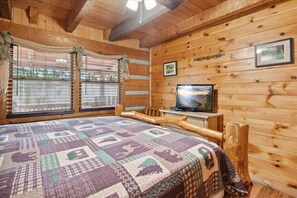 Una habitación tipo cabaña de madera con una cama, un televisor y una ventana con persianas.