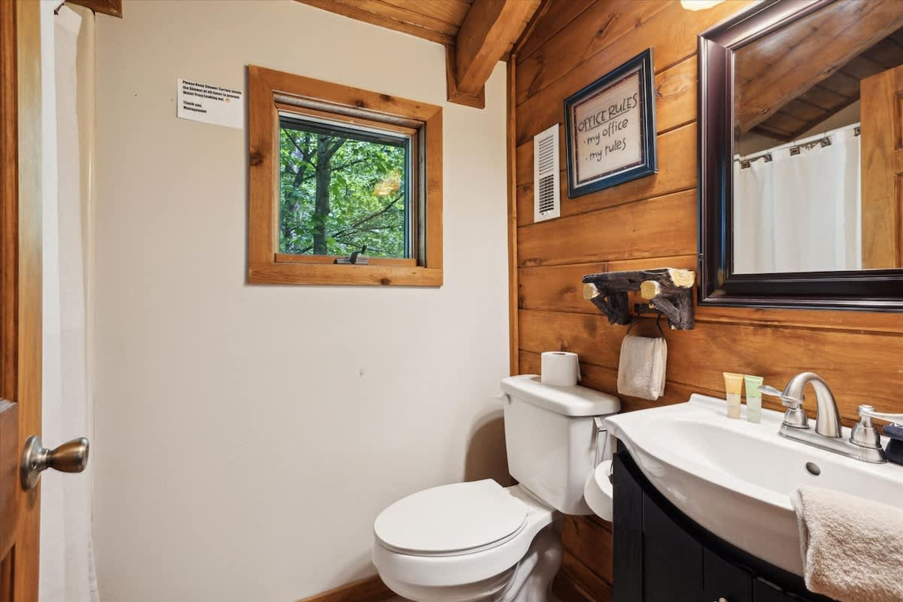 Een houten badkamer met toilet, wastafel en raam.