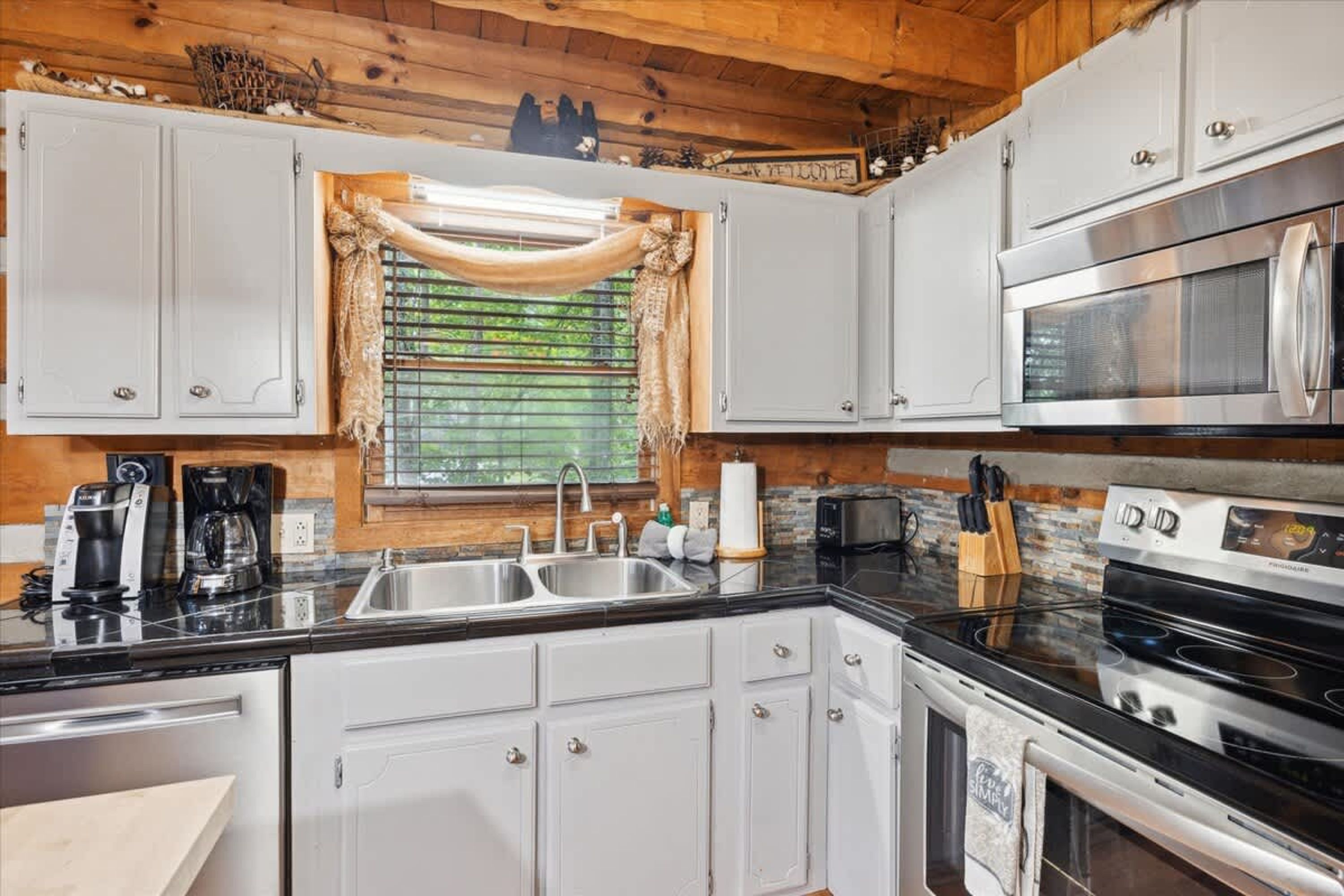 A kitchen with white cabinets, a stainless steel range, a microwave, and a window with a view of greenery.