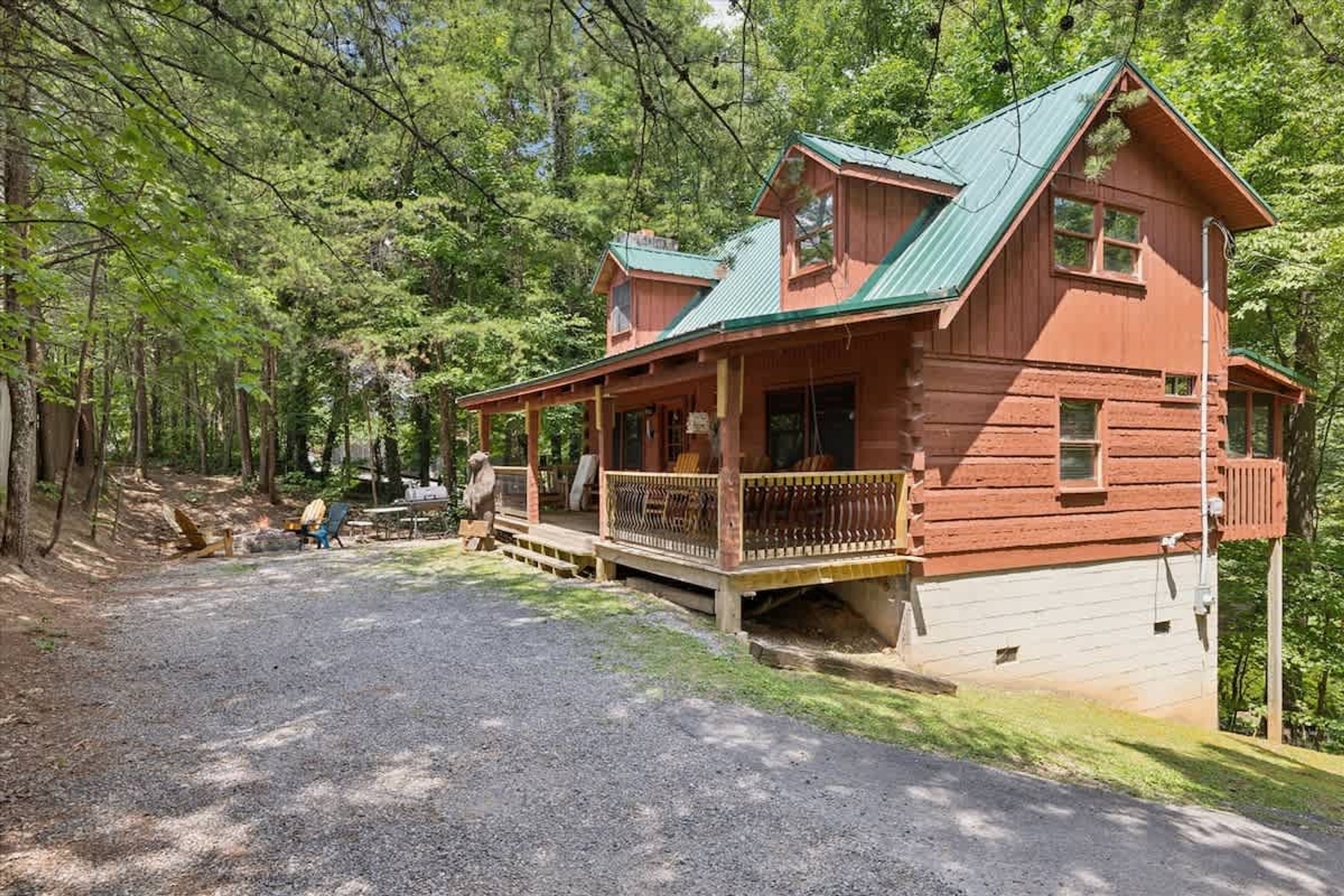 A rustic cabin with a porch, a chimney, and a gravel driveway.