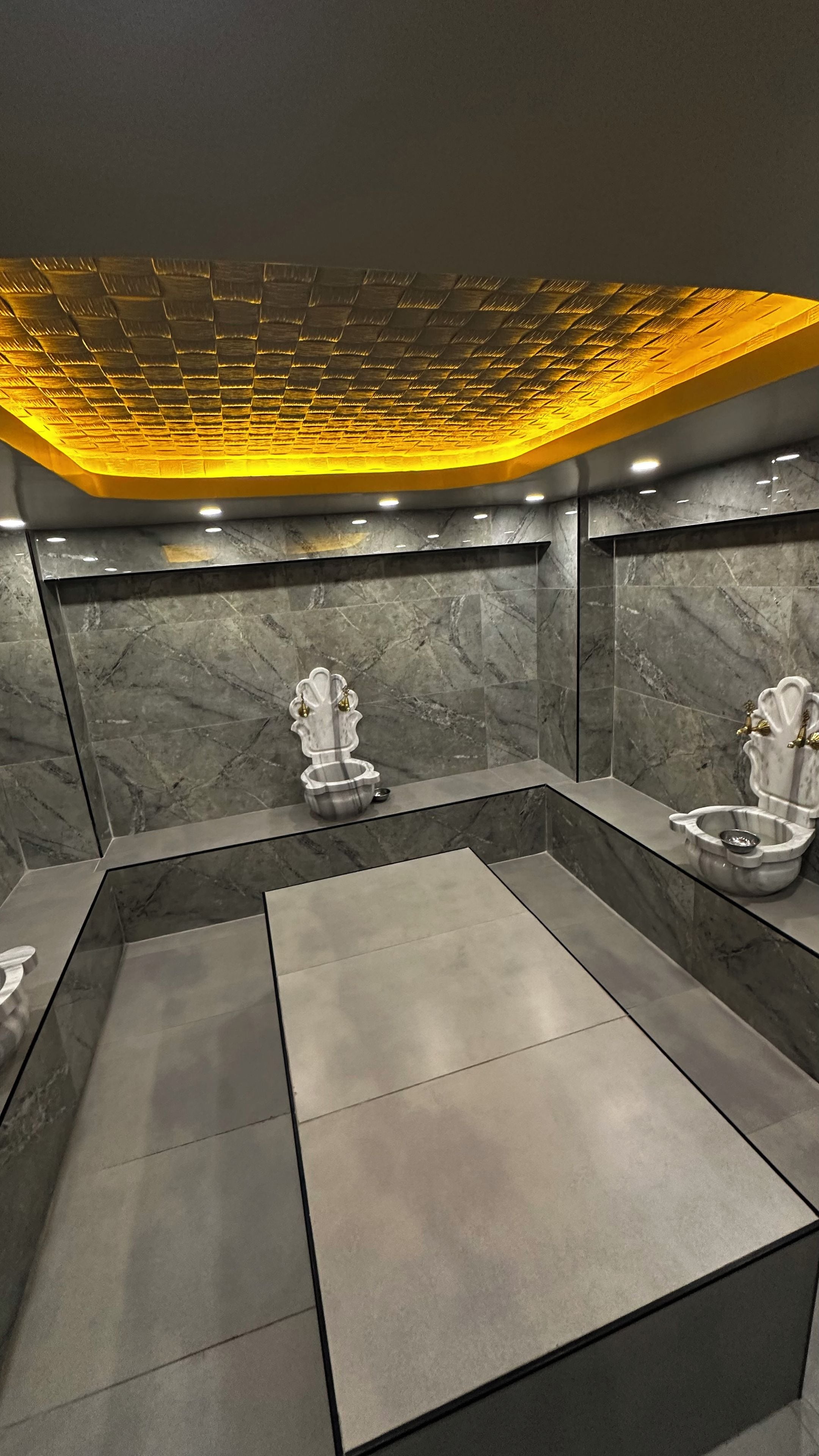 Un baño moderno con paredes de mármol, un diseño geométrico en el suelo y una lámpara de techo original.
