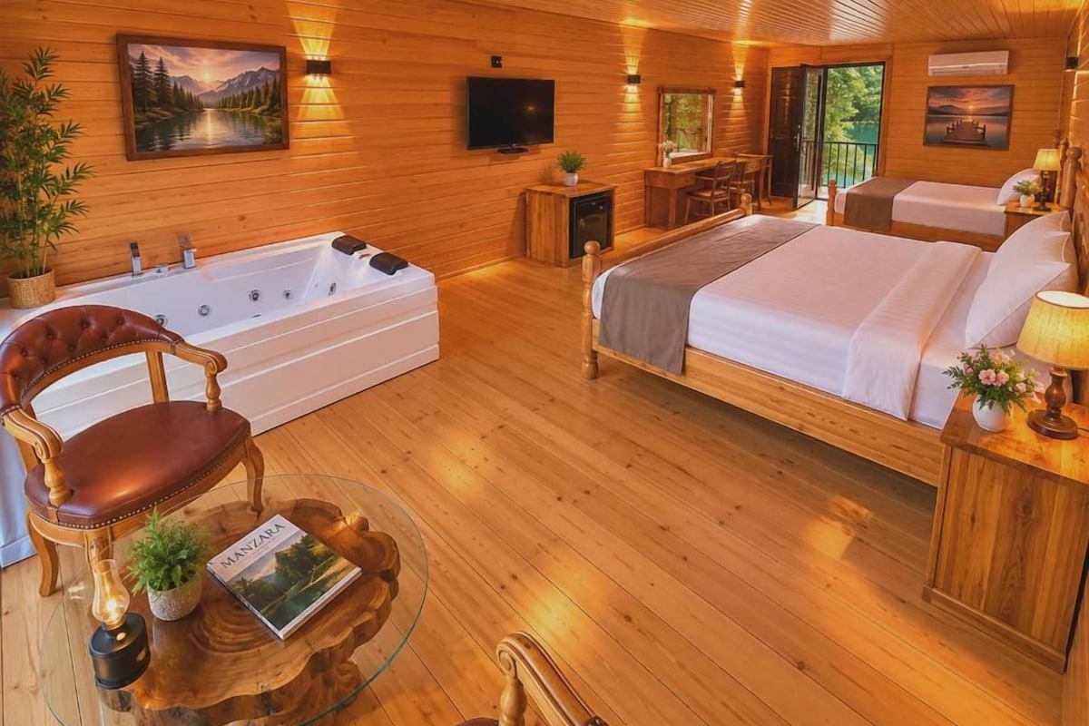 Interior de una cabaña de madera con una cama grande, un rincón de descanso con una silla y una mesa, una bañera y un televisor.