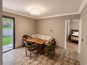 A room with a dining table and chairs, a sofa, a radiator, and a bed.