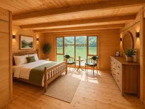 Un dormitorio de cabaña de madera con una cama, mesita de noche, sillas y vista a un lago.