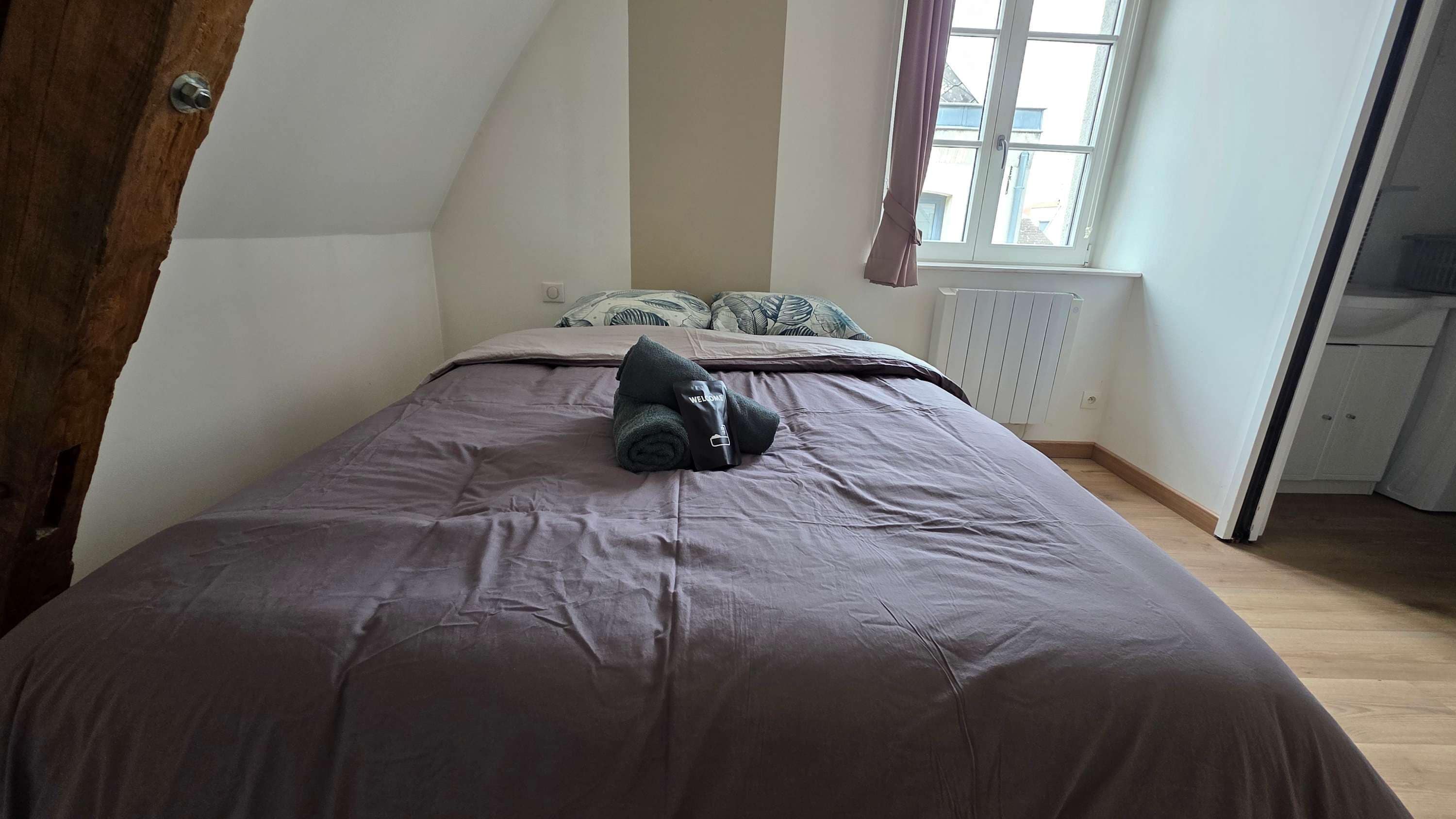 A bedroom with a bed, a radiator, and a window with curtains.
