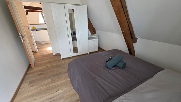 A bedroom with a bed, a wardrobe, and a wooden ceiling beam. - T2 l Gant Devant la Mairie - Calme - Centre (Arras)