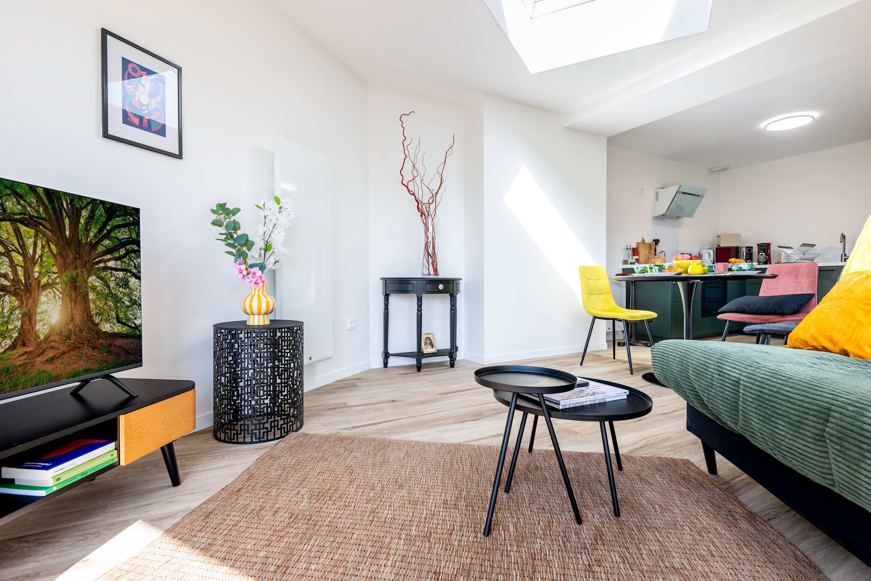 Een moderne woonkamer met een flatscreen televisie, een bank, een eettafel en een keuken in de achtergrond.