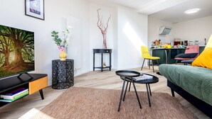 Ein modernes Wohnzimmer mit Flachbildfernseher, einer Couch, einem Esstisch und einer Küche im Hintergrund.