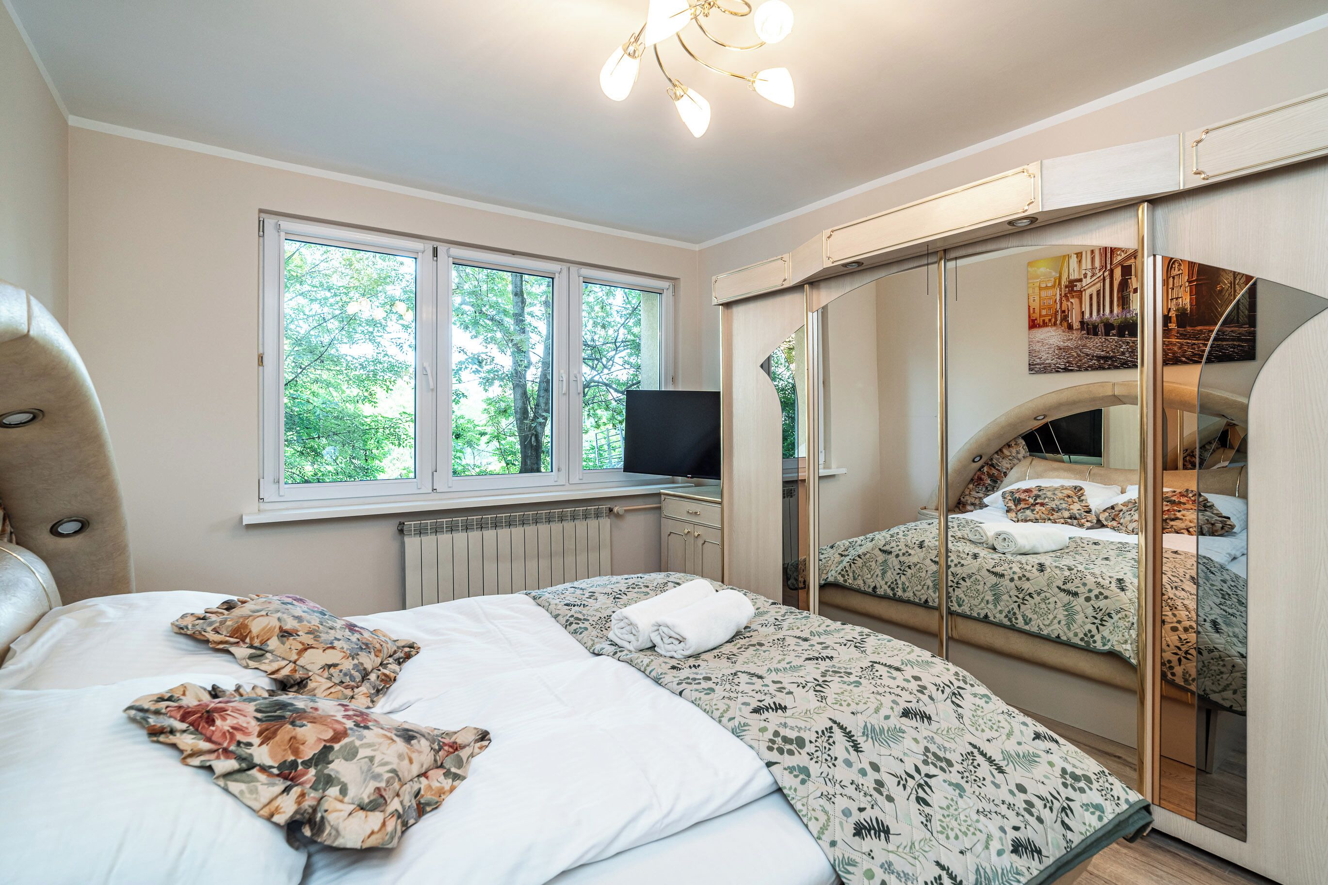 A bedroom with a bed, a television, a window, and a mirror.