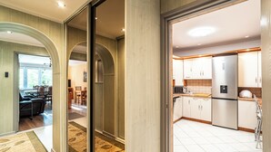 A modern kitchen with stainless steel appliances, a dining area with a table and chairs, and a hallway with wooden flooring and a carpet. - RentPlanet - Apartament Weissa (Kraków)