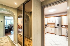 A modern kitchen with stainless steel appliances, a dining area with a table and chairs, and a hallway with wooden flooring and a carpet. - RentPlanet - Apartament Weissa (Kraków)
