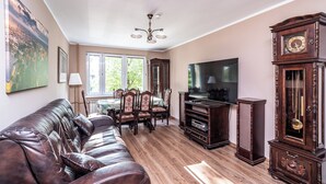 A living room with a leather sofa, a dining table with chairs, a flat-screen TV, a grandfather clock, and a painting on the wall. - RentPlanet - Apartament Weissa (Kraków)