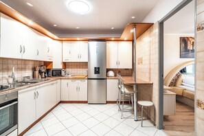A modern kitchen with stainless steel appliances, white cabinetry, and a tiled floor. - RentPlanet - Apartament Weissa (Kraków)
