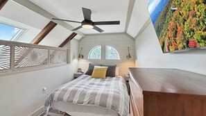 Ein Schlafzimmer mit Bett, Deckenventilator, Nachttisch, Lampe und einem großen Fenster.