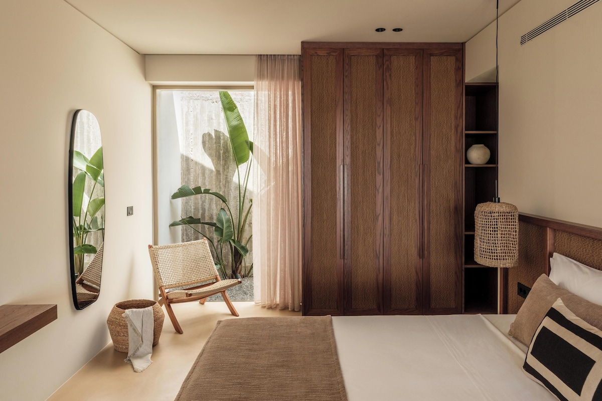 A bedroom with a bed, a chair, a wardrobe, and a large window with curtains.