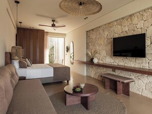 A modern living room with a stone wall, a flat-screen TV, a ceiling fan, and a dining area with a round table. - Filema Suites (Xirokampi)