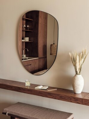 A bathroom with a wooden vanity, a round mirror, a sink, and a vase with dried plants. - Filema Suites (Xirokampi)