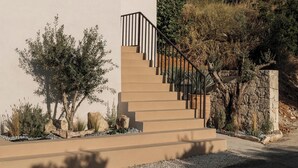 Un bâtiment moderne à l’extérieur beige, avec un escalier doté de rampes noires, et un ciel bleu clair parsemé de nuages.