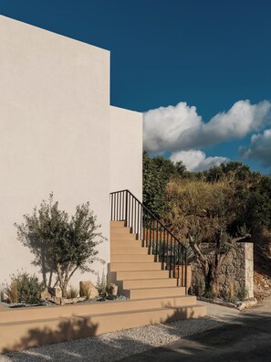 A modern building with a beige exterior, a staircase with black railings, and a clear blue sky with clouds. - Filema Suites (Xirokampi)