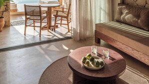 Une pièce avec un mur en pierre, un canapé, une table ronde sur laquelle se trouve une assiette de fruits, et une vue sur une piscine et des montagnes.
