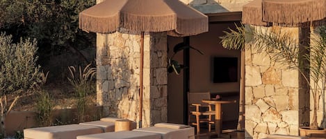 A poolside area with stone walls, lounge chairs, and umbrellas.