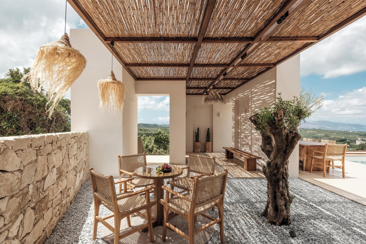 An outdoor seating area with wicker furniture, a central table with fruit, and a view of the landscape.