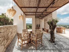 An outdoor seating area with wicker furniture, a central table with fruit, and a view of the landscape. - Filema Suites (Xirokampi)
