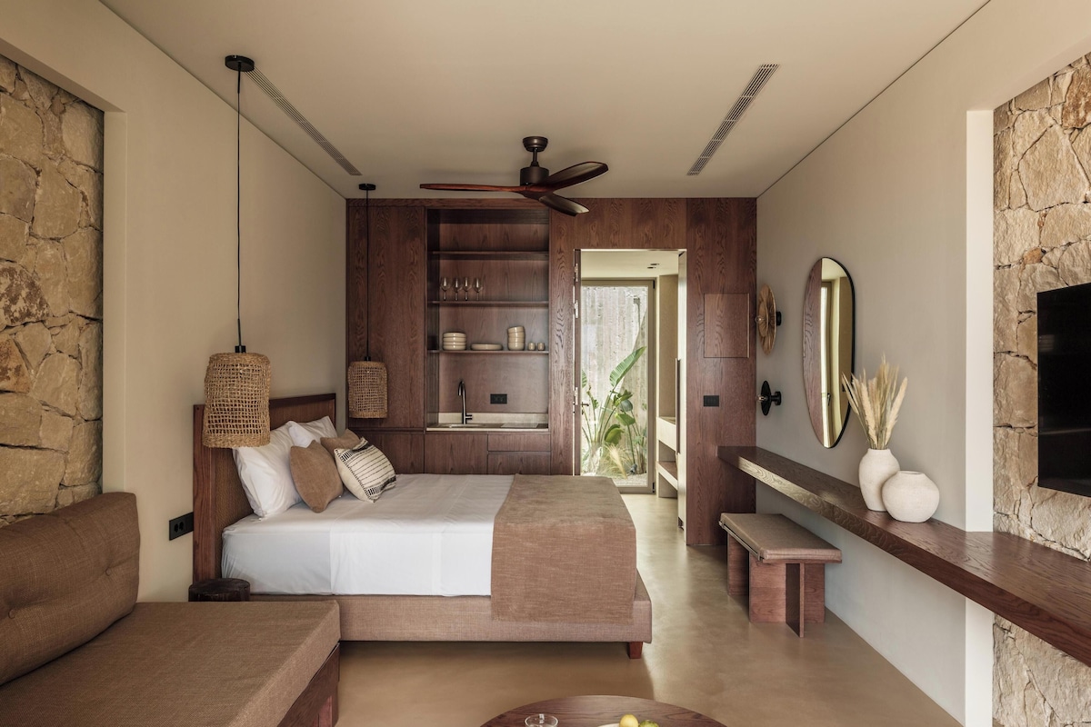 A modern bedroom with a bed, a seating area, a dining table, and a built-in kitchen.