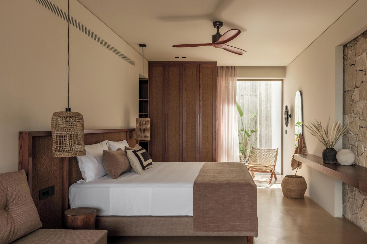 A modern bedroom with a large bed, a ceiling fan, a wooden wardrobe, and a view of the outdoors.