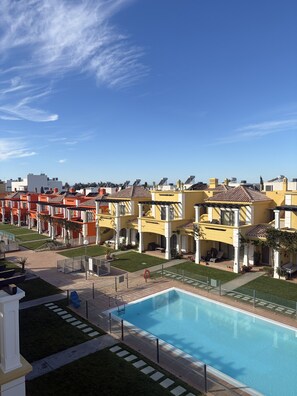 A residential area with a swimming pool, multiple houses with balconies, and a clear sky. - Homely Lux Tavira | Premium Villa with Pool near Tavira and the Beaches (Luz)