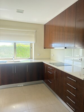 A modern kitchen with dark wood cabinets, a white countertop, and a window with a view of greenery. - Homely Lux Tavira | Premium Villa with Pool near Tavira and the Beaches (Luz)