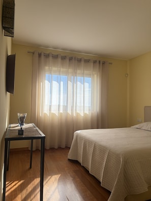 A bedroom with a bed, a table with a vase, and a window with curtains. - Homely Lux Tavira | Premium Villa with Pool near Tavira and the Beaches (Luz)