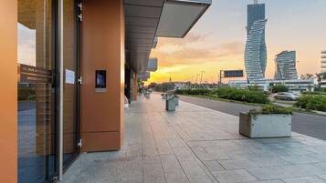 Ein modernes Gebäude mit Glasfassade, blauem Himmel und weiter Ansicht eines hohen Wolkenkratzers in der Ferne.