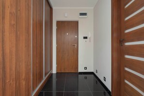A hallway with a wooden door, a white wall-mounted thermostat, and a black-tiled floor. - Practical Family Apartment | 2 Bedrooms | Close to the Airport (Warszawa)