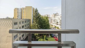 A view from a balcony overlooking a cityscape with multiple buildings, a parking area, and a tree. - Practical Family Apartment | 2 Bedrooms | Close to the Airport (Warszawa)