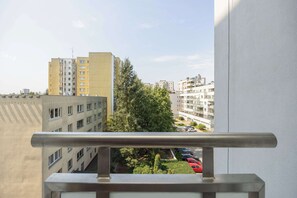 A view from a balcony overlooking a cityscape with multiple buildings, a parking area, and a tree. - Practical Family Apartment | 2 Bedrooms | Close to the Airport (Warszawa)