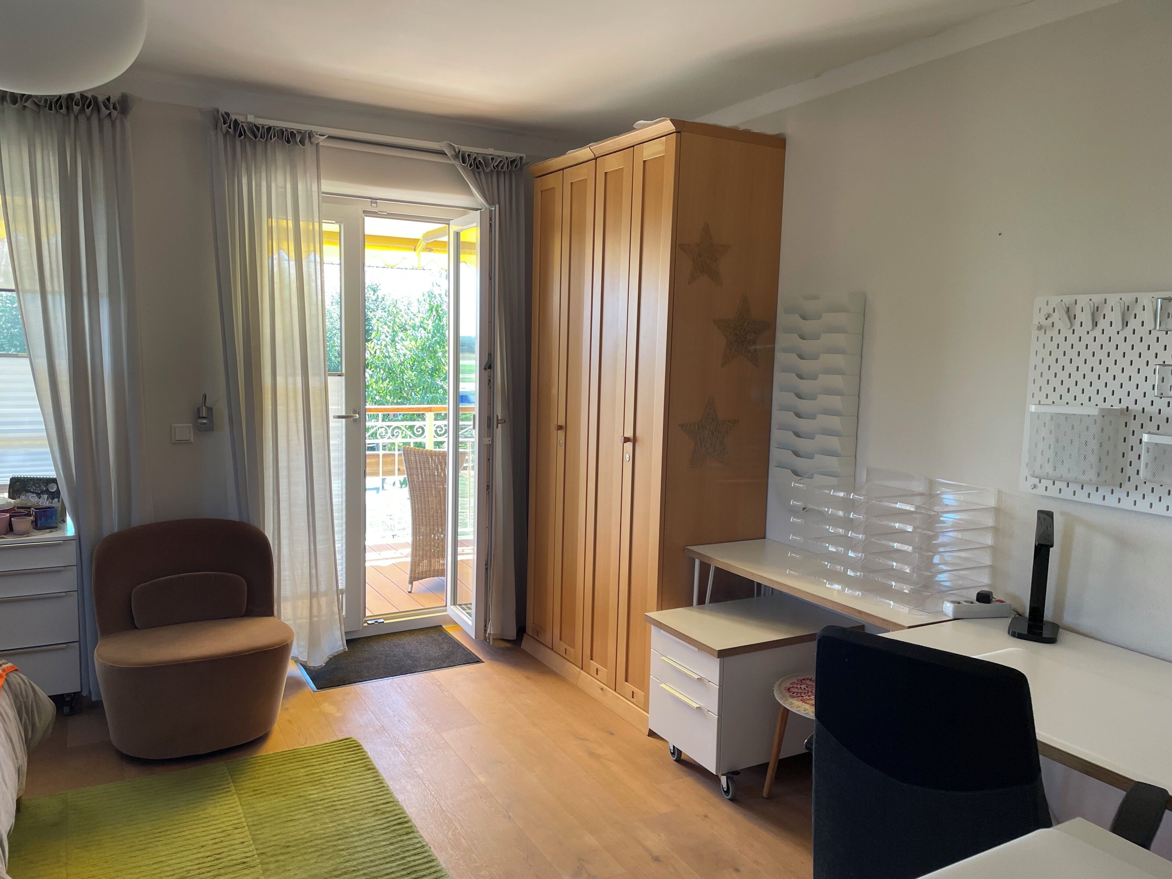 Habitación con escritorio, silla, armario y vistas a un espacio exterior por una puerta.