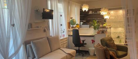 A modern living room with a sofa, a chair, a desk, and a kitchen area with shelves and a globe.