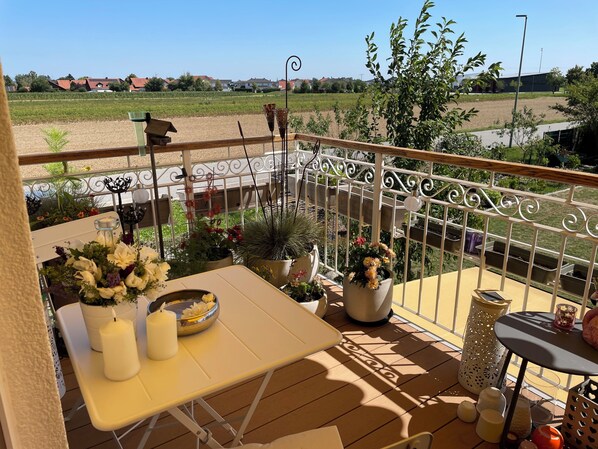 Un balcon avec une table, des chaises, des plantes en pot et une rambarde.