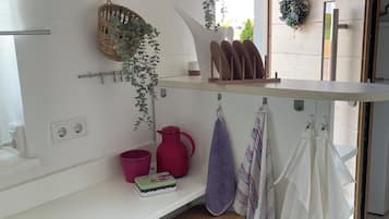 A modern kitchen with white cabinetry, hanging baskets with plants, a wooden countertop, and a window providing natural light.