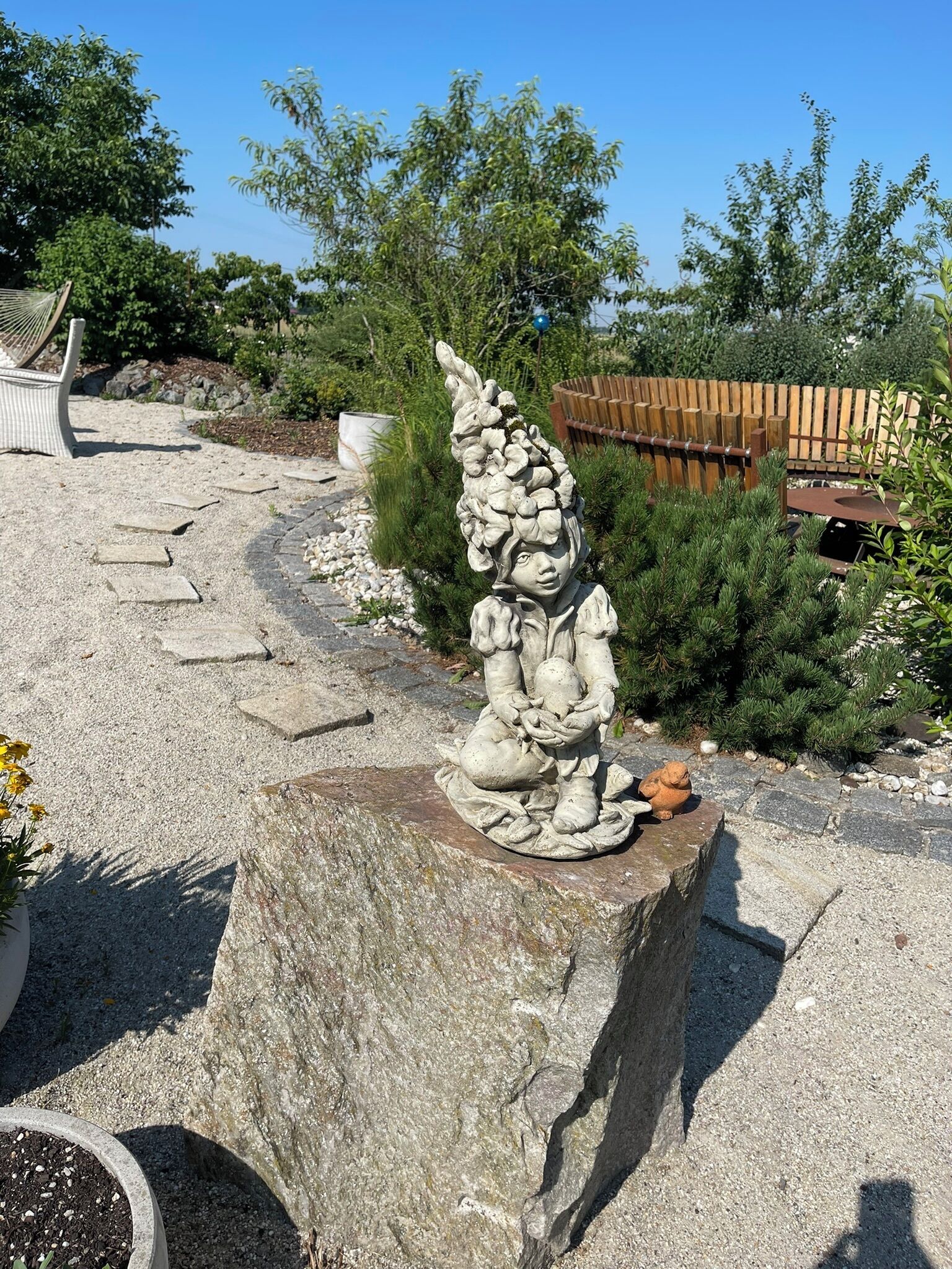 Eine Gartenstatue eines Kindes, das eine Blume hält, auf einem Steinsockel platziert.