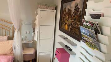 Une chambre à coucher avec un lit, une armoire, un bureau, une chaise, une boîte rose, une télécommande et un tableau encadré accroché au mur.