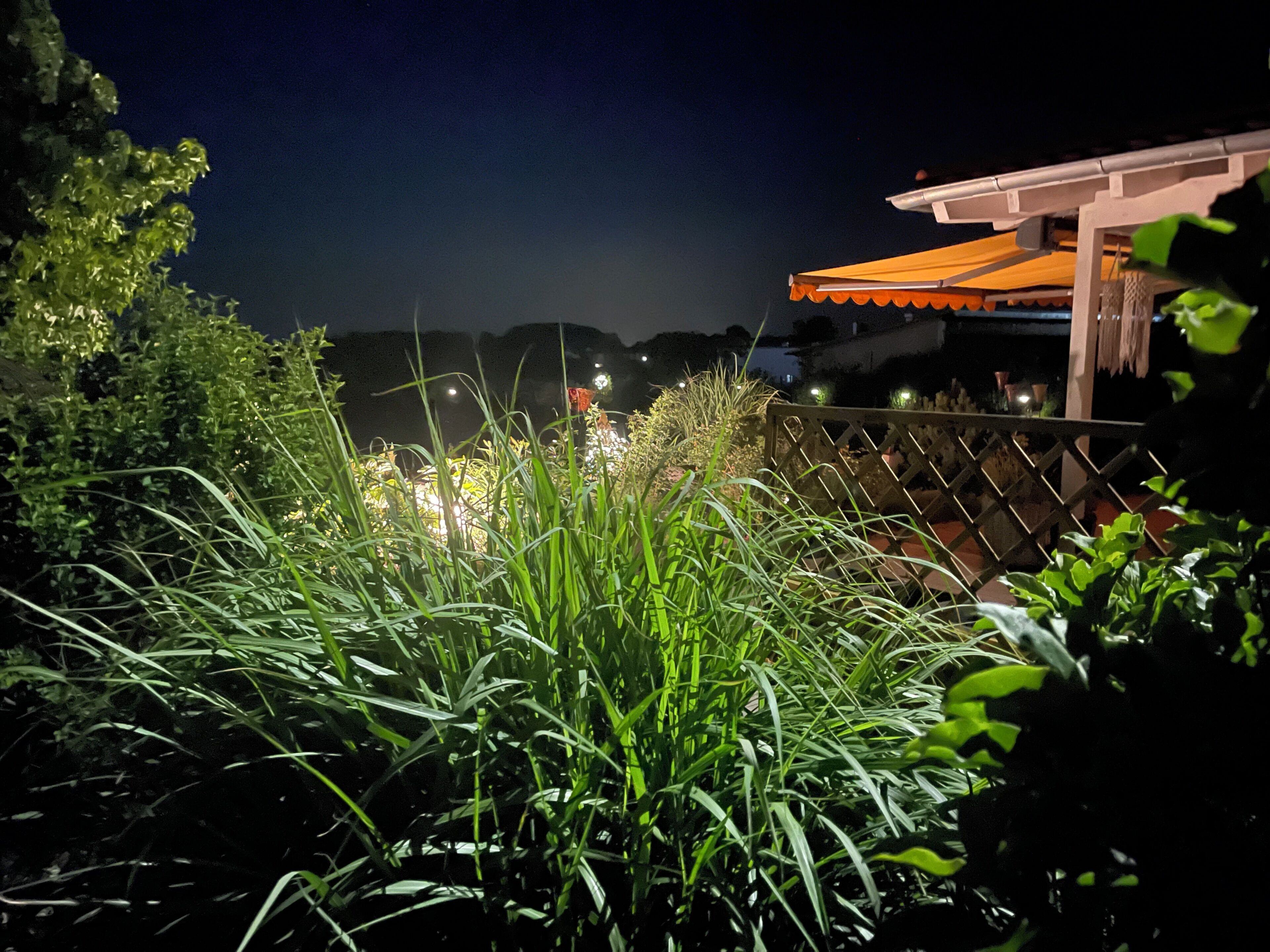 Ein Gartenbereich mit Holzfence, einer Pergola mit orangem Baldachin und Blick auf den Nachthimmel.